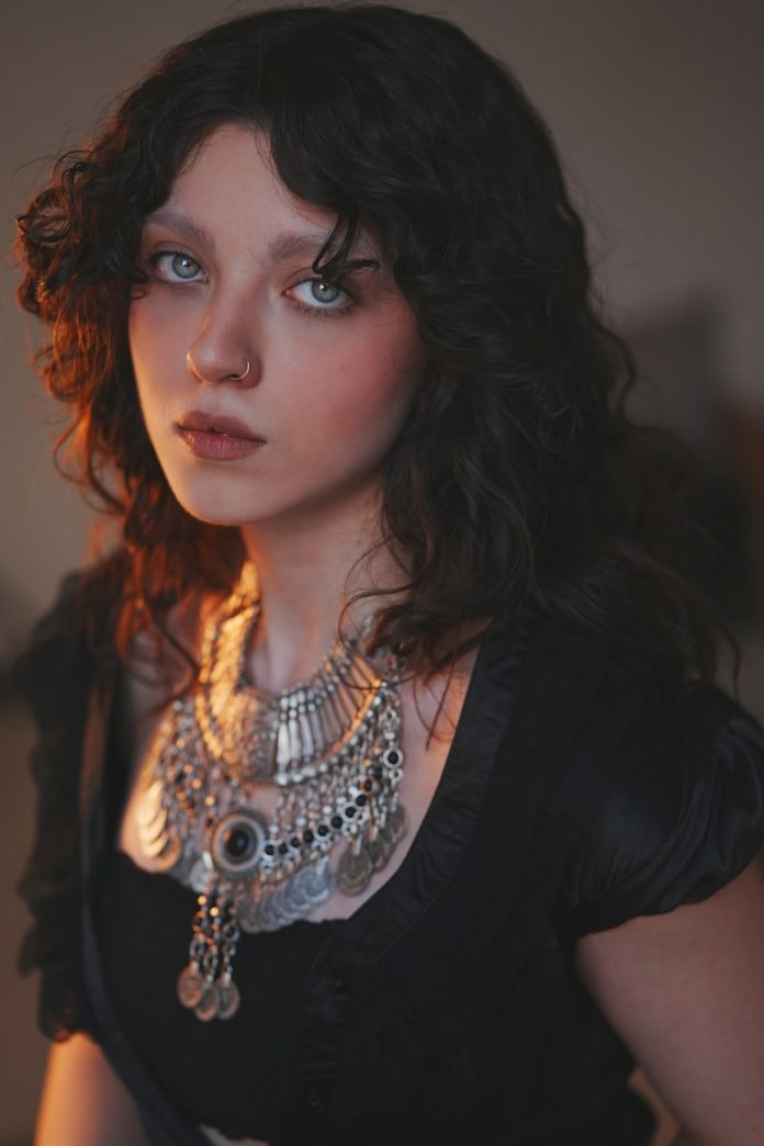 Young woman with dark curly hair and striking necklace.