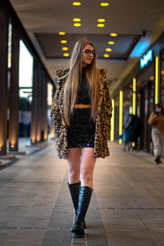 woman in brown leopard coat and black leather boots walking on sidewalk during daytime